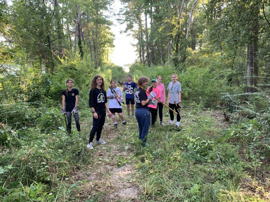 Members of the cross country team work together to clear a path for running in the woods on school property.